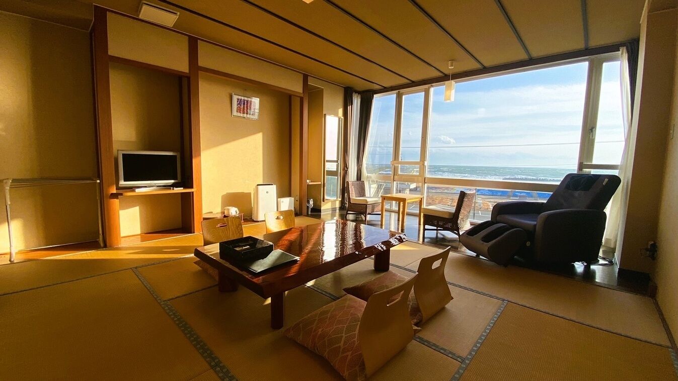 A room with tatami flooring, a television, a dining table, and a view of the ocean.