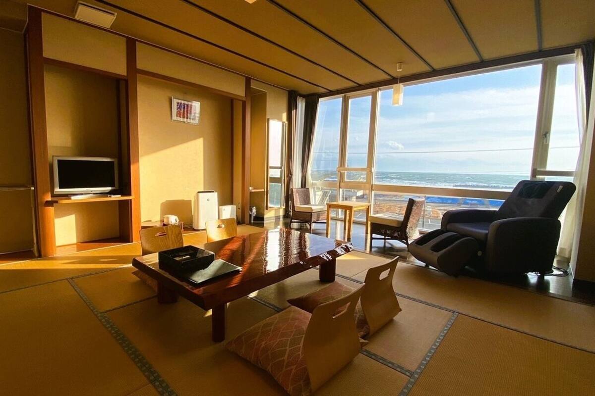 Habitación con suelo de tatami, televisión, mesa de comedor y vista al océano.