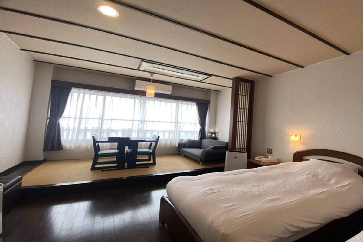 Una habitación de hotel con cama, escritorio, silla, sofá y ventana con cortinas.