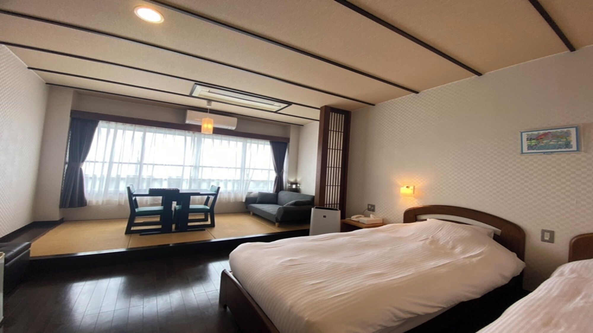 A hotel room with a bed, a desk with a chair, a sofa, and a large window with curtains.