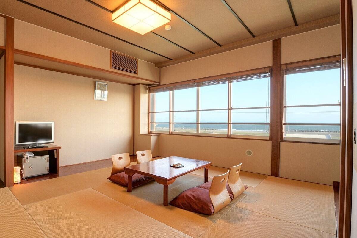 Una habitación tradicional japonesa con suelo de tatami, televisión y vista al mar.