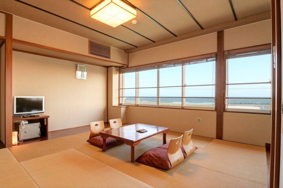 Una habitación japonesa tradicional con suelo de tatami, un televisor, una mesa con cojines y un gran ventanal con vistas.