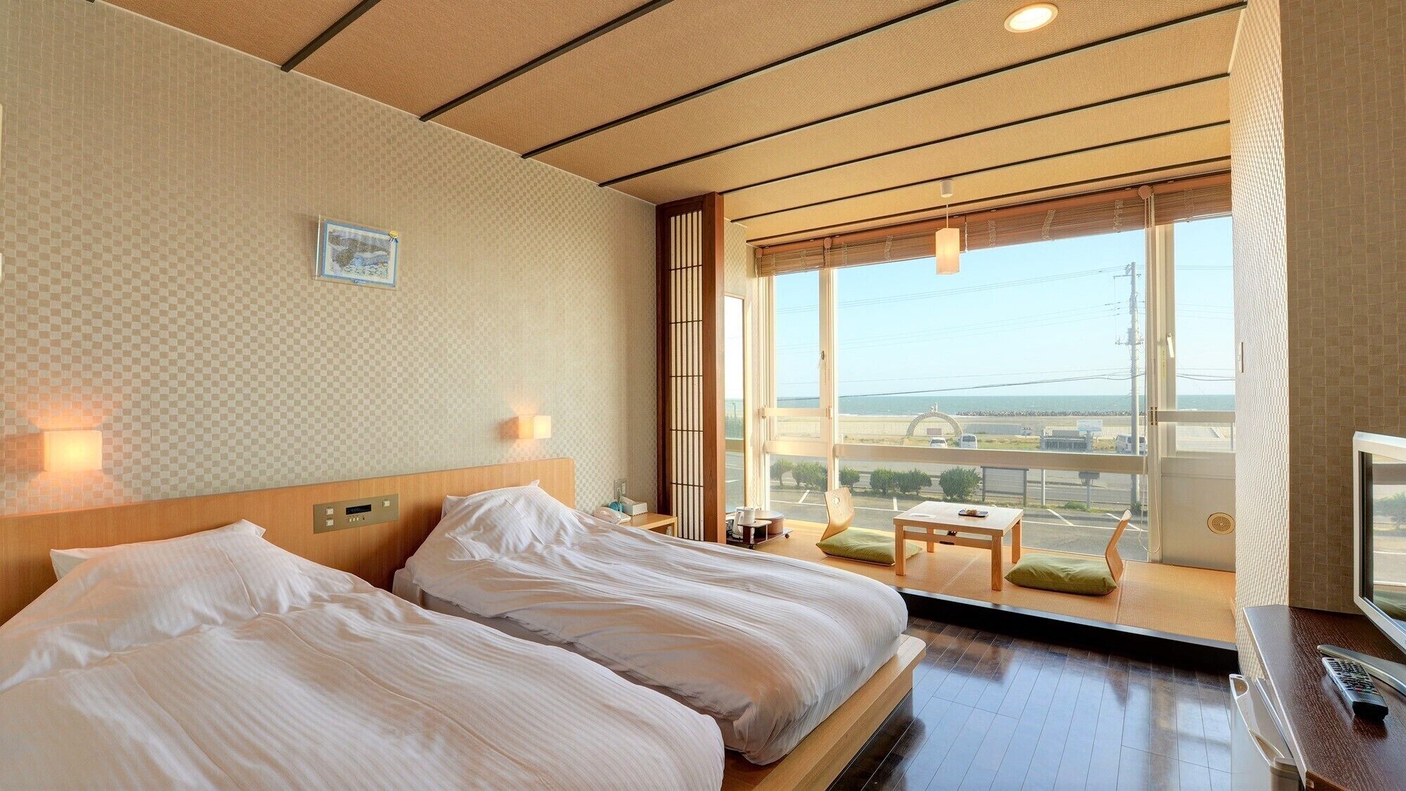 A hotel room with two beds, a TV, a window with a view, and a small table.