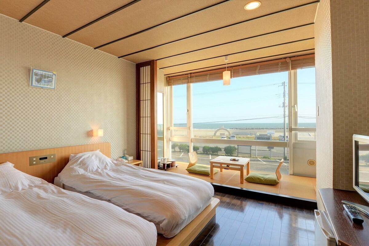 Habitación de hotel con dos camas, televisión, ventana con vistas y una mesita.