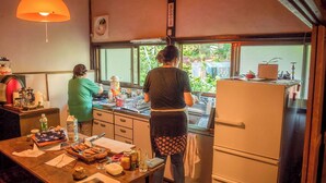 Una cocina con dos personas cocinando, un refrigerador, un fregadero y una ventana que da a vistas de follaje exterior.