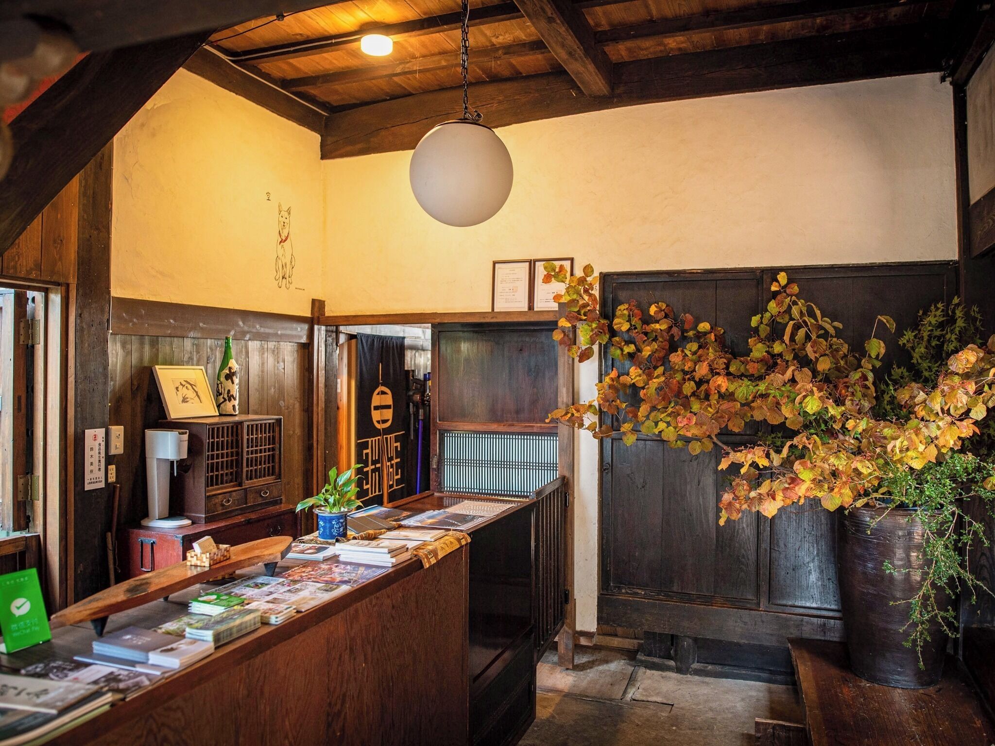 A wooden interior with a reception desk, books, a hanging light, and autumn leaves.