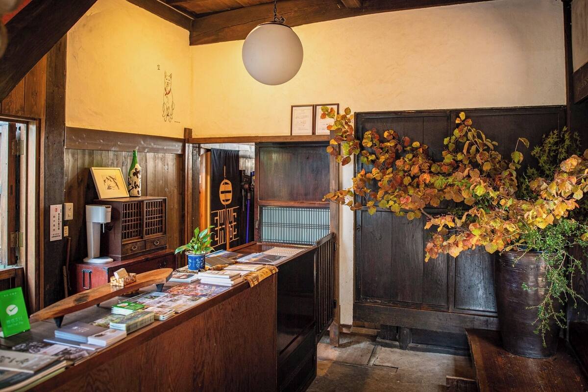 Interior de madera con mostrador de recepción, libros, una lámpara colgante y hojas de otoño.