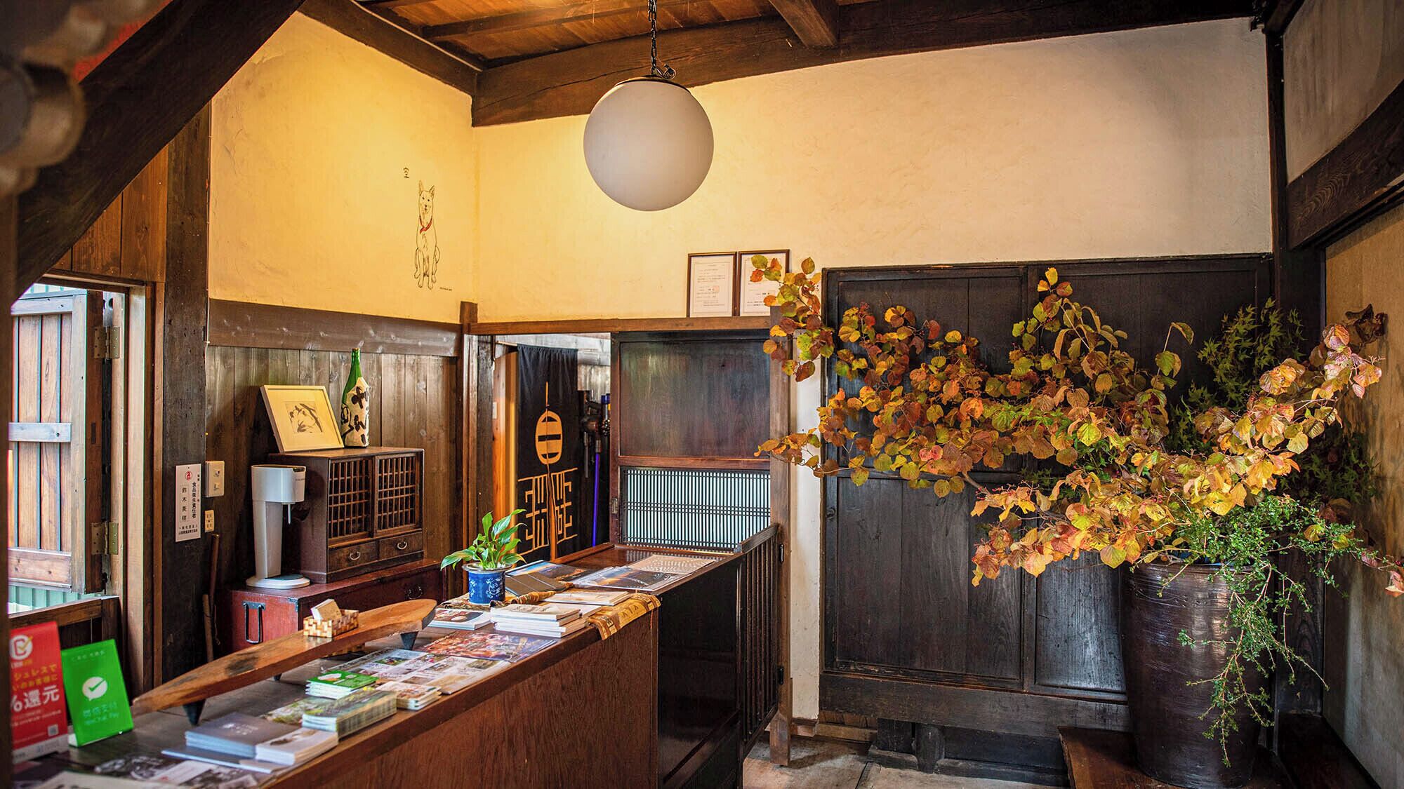 A traditional Japanese inn with a wooden reception desk, a hanging light fixture, and autumn foliage.