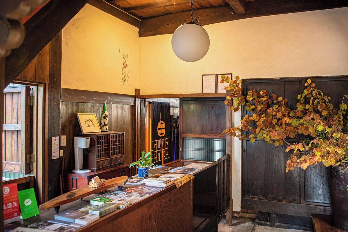 Una posada japonesa tradicional con mostrador de recepción de madera, una lámpara colgante y follaje otoñal.