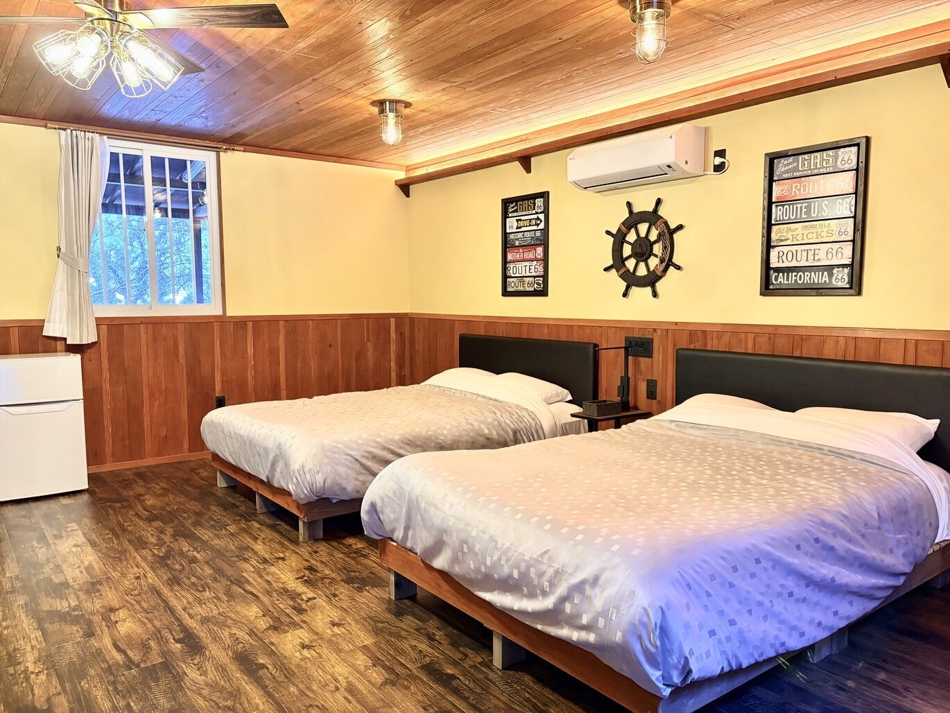 Una habitación con dos camas, paneles de madera, decoración con timón de barco y señales de la Ruta 66.