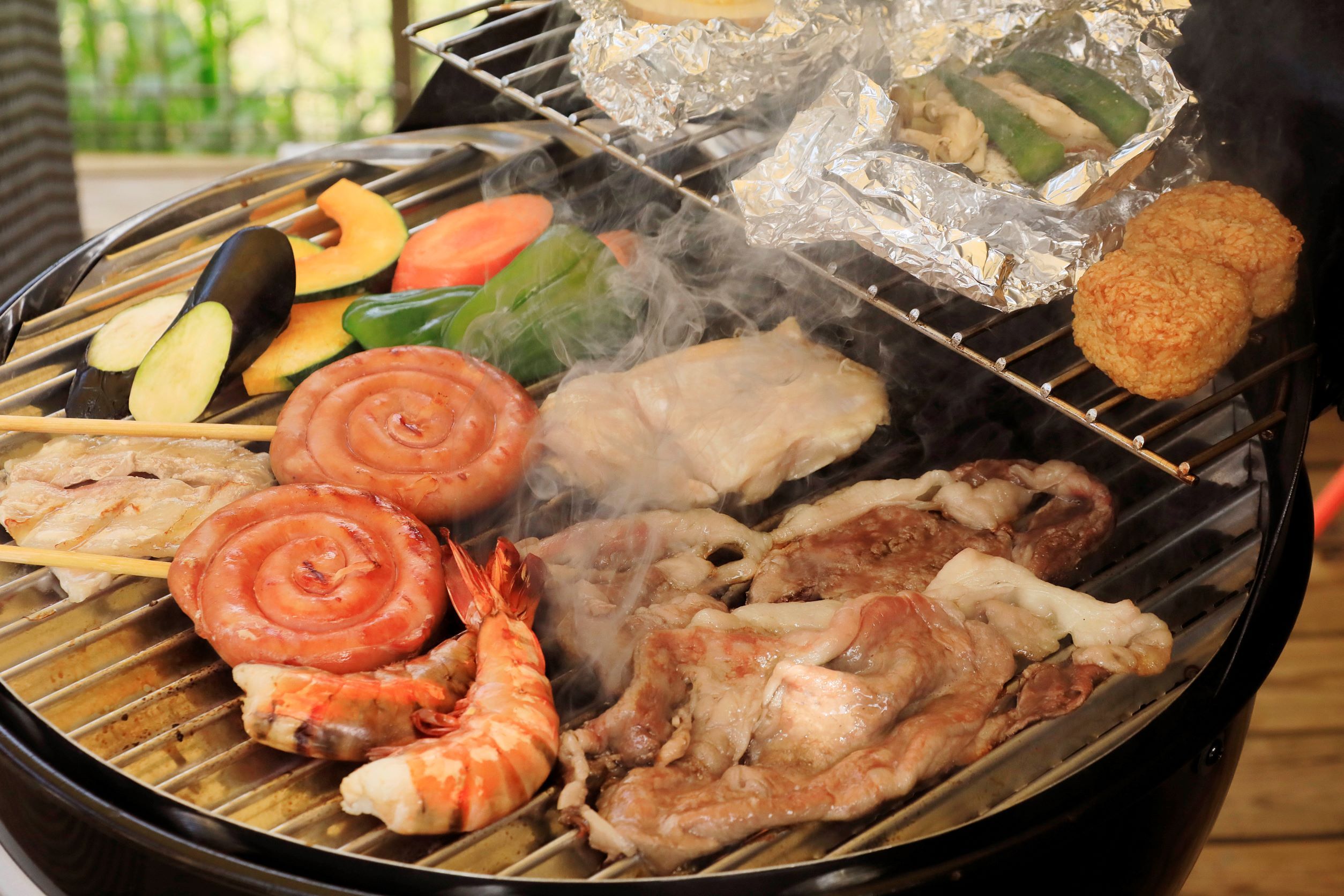 A variety of meats and vegetables being grilled on an outdoor grill.