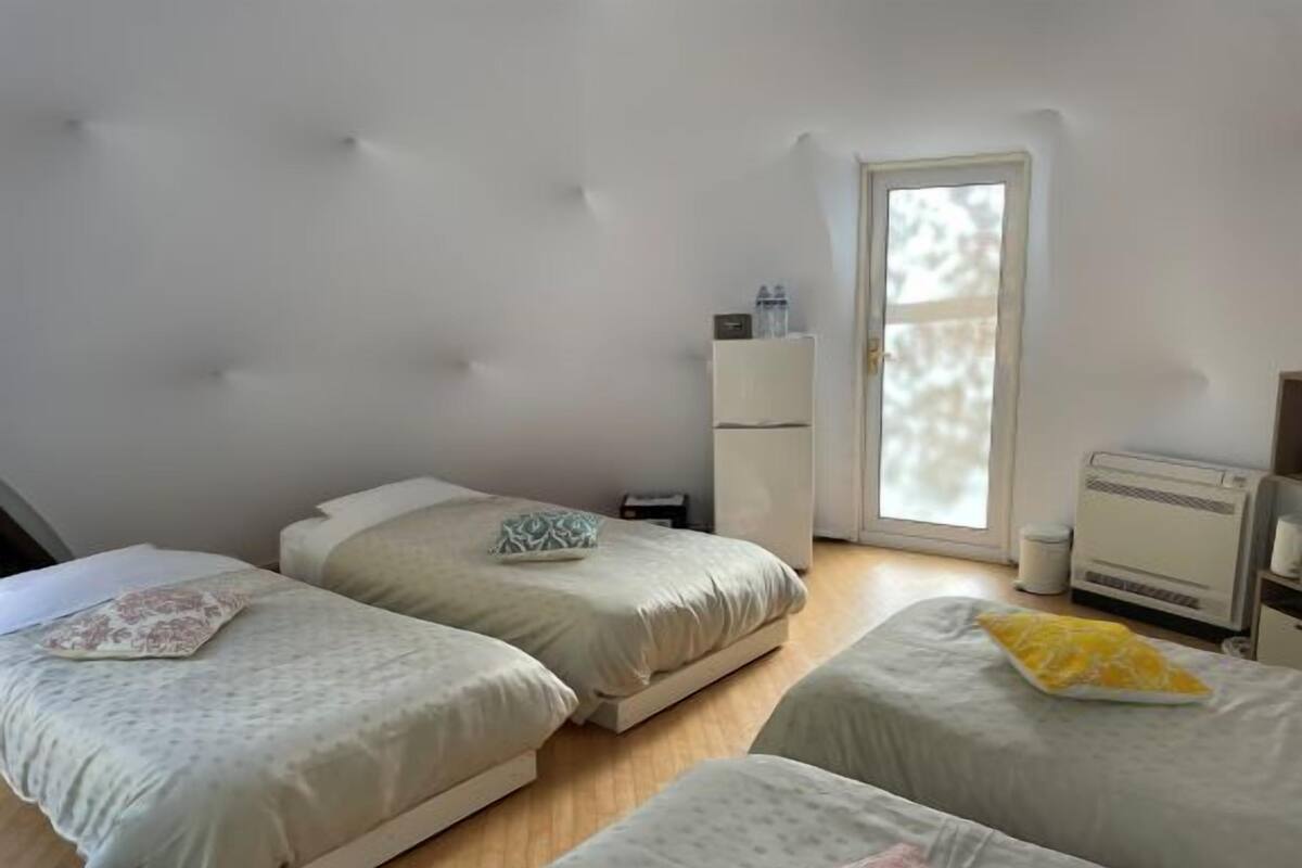 A room with three beds, a wardrobe, a radiator, and a door to a balcony.