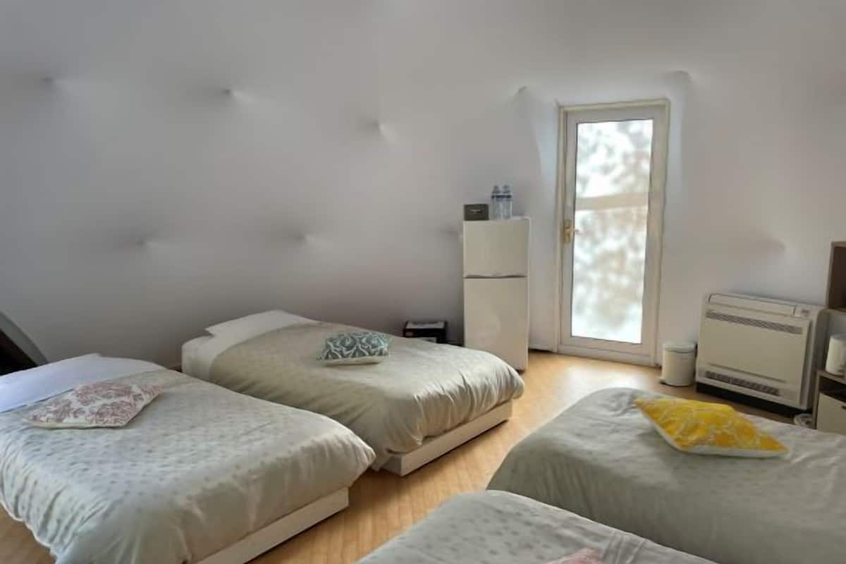 Ein Zimmer mit drei Betten, einem Kleiderschrank, einem Heizkörper und einer Balkontür.