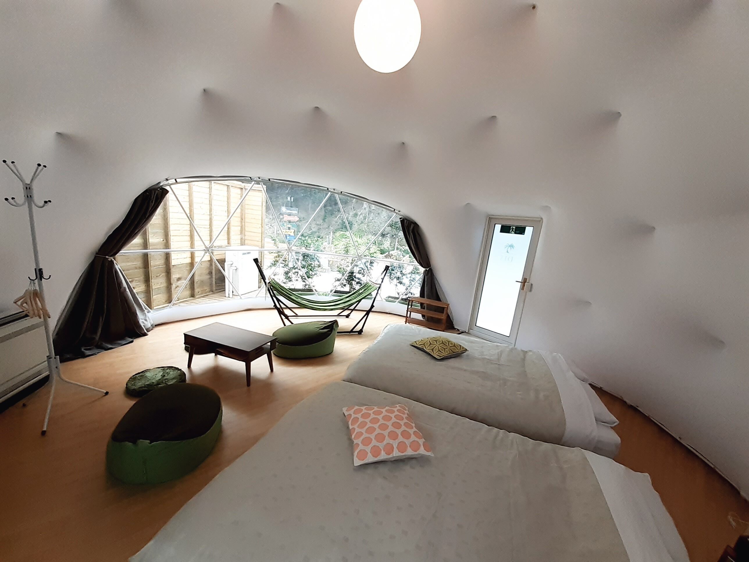Una habitación acogedora y circular con una cama, una silla, una hamaca y vistas al verdor exterior.