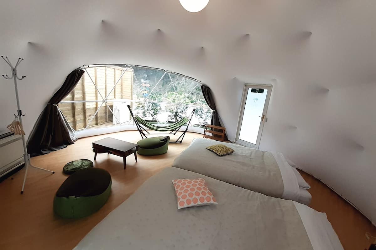 Una habitación acogedora y circular con una cama, una silla, una hamaca y vistas al verdor exterior.