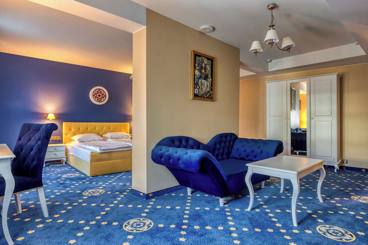 Une chambre d’hôtel avec un lit, un canapé bleu, une table blanche et un tapis à motifs.