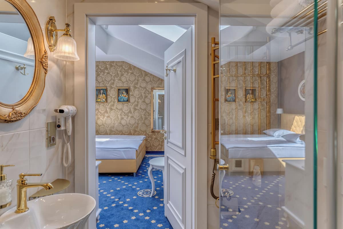 Une chambre d’hôtel avec un grand miroir, un téléphone sur la table de chevet, un lit recouvert d’une moquette à motifs floraux bleus et une petite salle de bain avec un lavabo et un miroir.