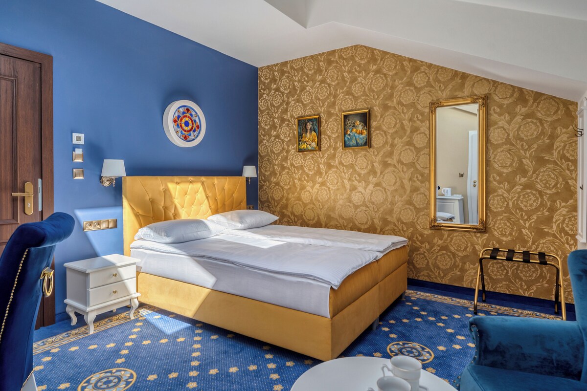 A hotel room with a large bed, a bedside table, a chair, and a small table with a cup and saucer.