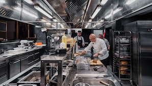 A commercial kitchen with stainless steel appliances, a large sink, and a rack of baked goods. - Czeczotka Palace Apartments (Kraków)