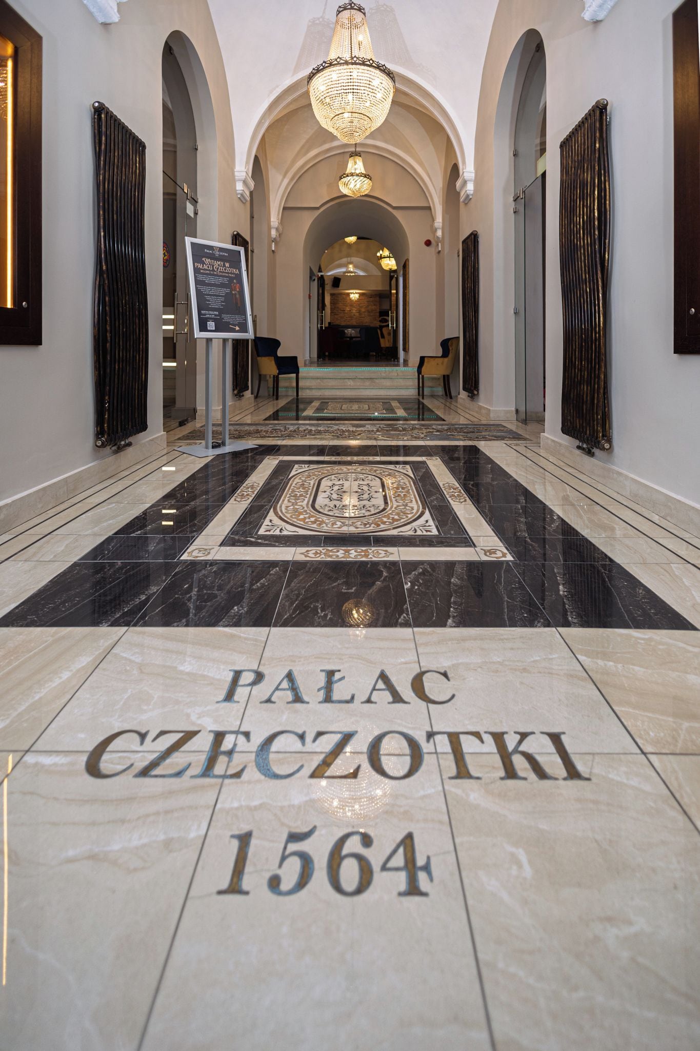 Un pasillo con suelo de mármol e inscripción 'PALACE CZECHOTKI 1564', que conduce a un gran arco.