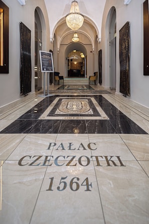 Un couloir au sol de marbre, sur lequel on peut lire l’inscription « PALACE CZECHOTKI 1564 », mène à une grande arche.