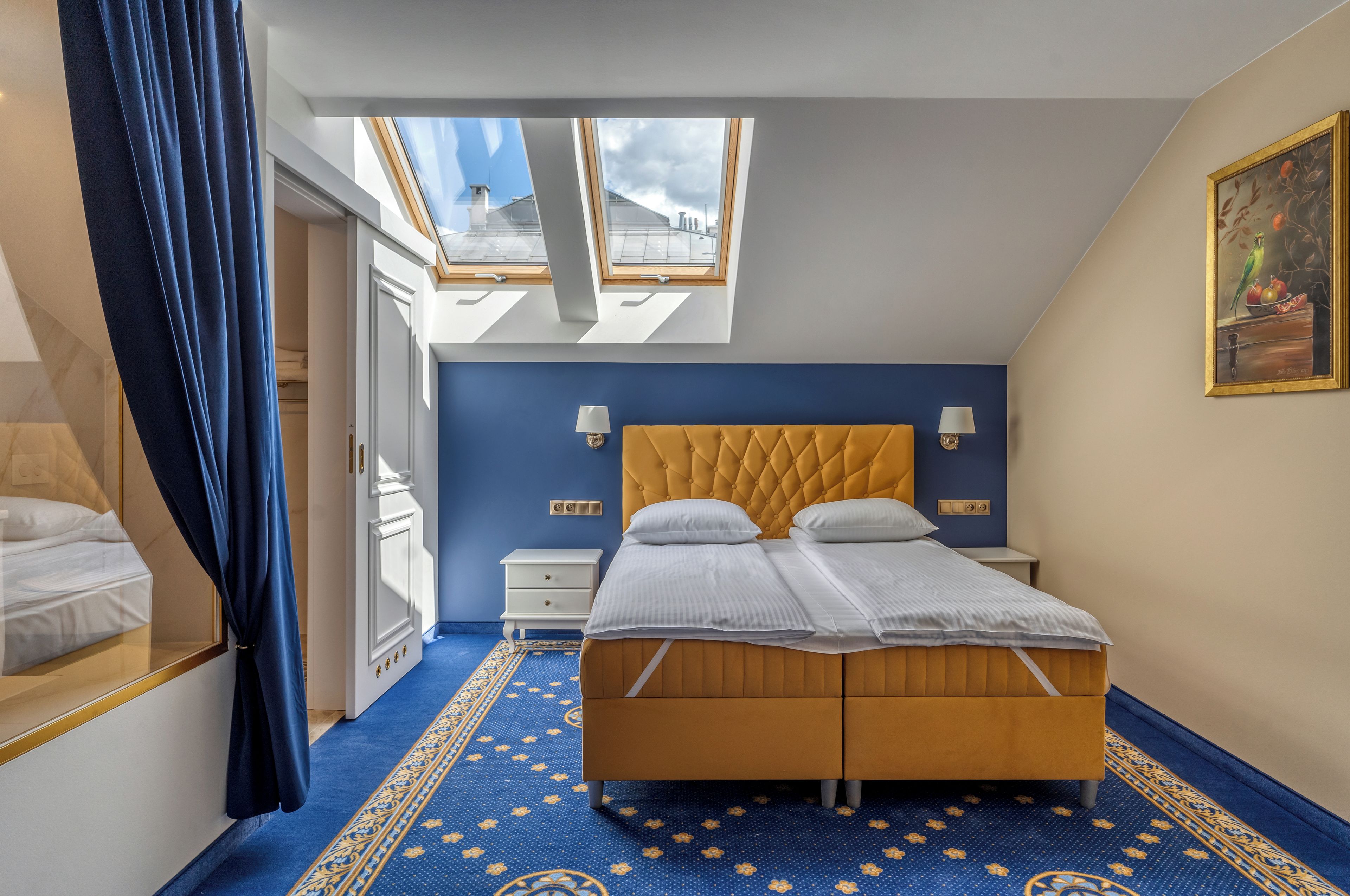A bedroom with a bed, skylight, and a painting on the wall.