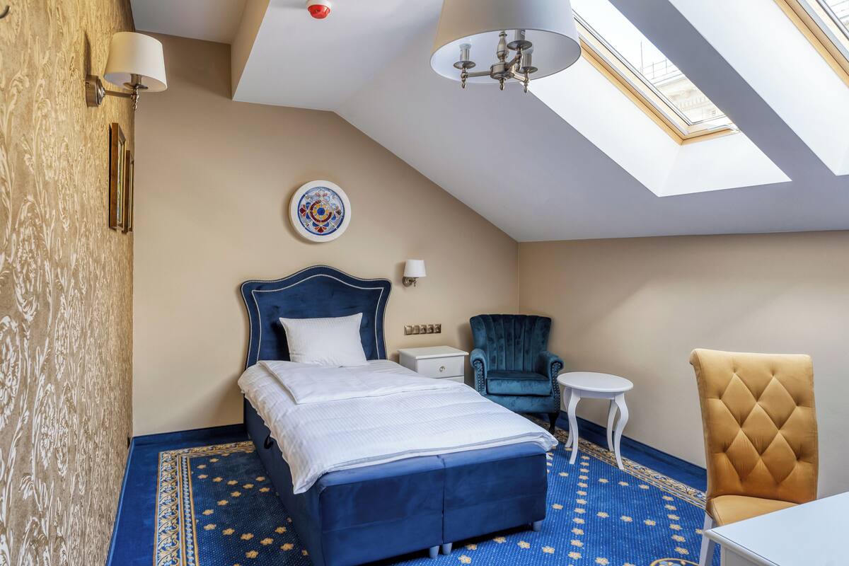 Une chambre à coucher avec un grand lit, une chaise bleue, une petite table et un lustre.