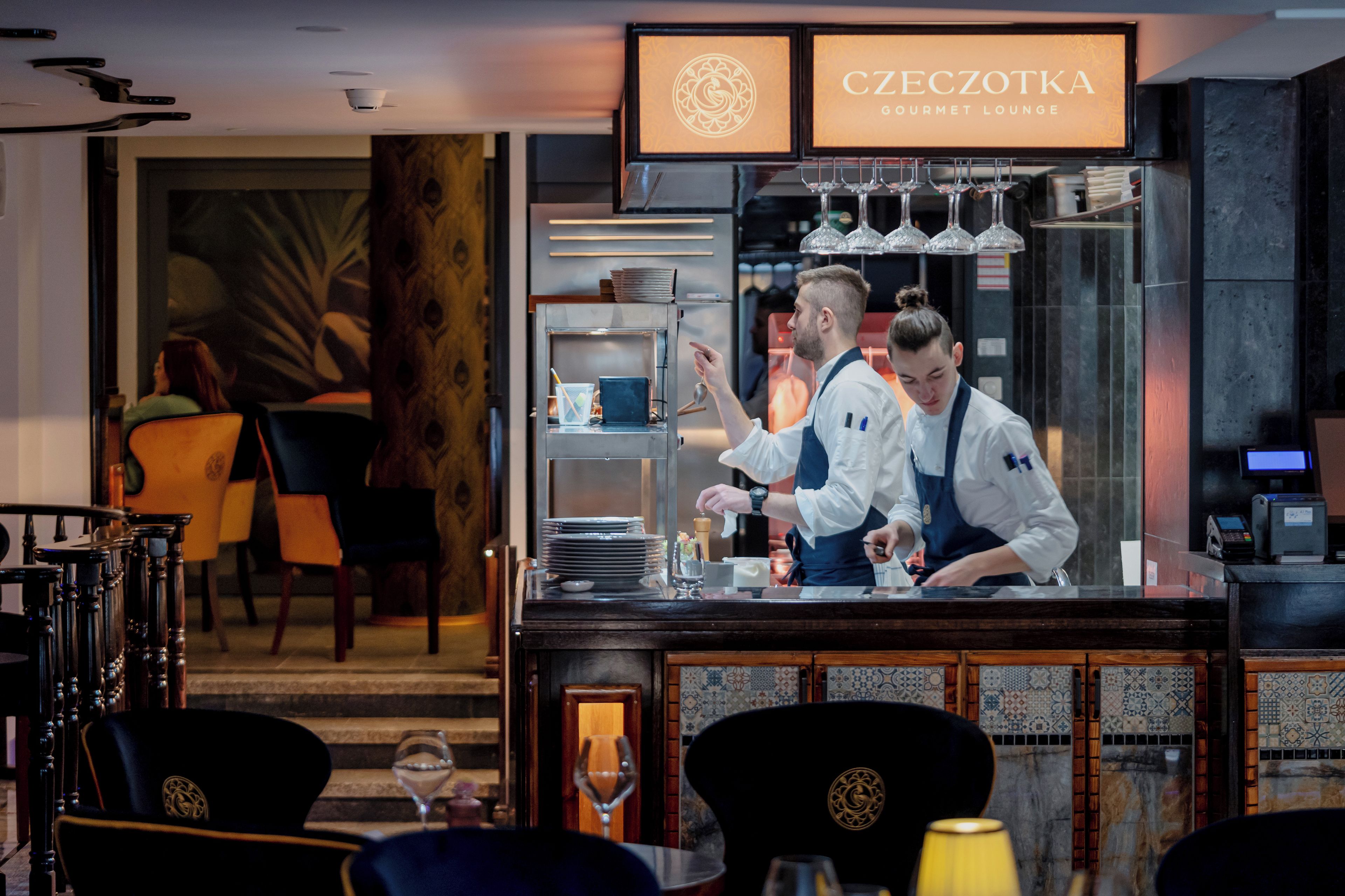 A bar area with a sign reading 'CZECHOTKA GOURMET LOUNGE,' a bar counter, and a seating area with chairs and a table.