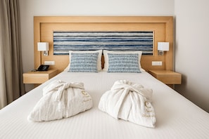 A hotel room with a large bed, two bedside lamps, a nightstand with a phone, and two towels with embroidered text. - Paradise Resort Evia (Eretria)