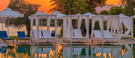 A poolside area with cabanas and lounge chairs, reflecting in the water.