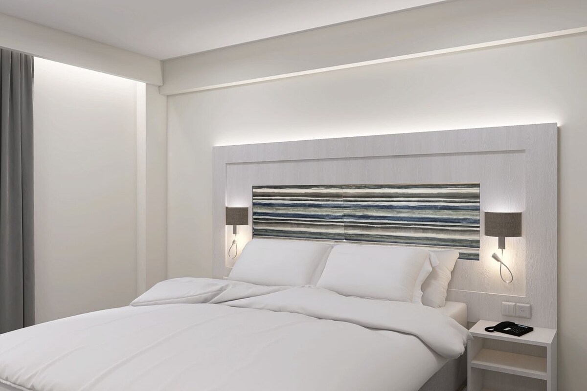Una habitación de hotel moderna con una cama grande, un cabecero con diseño texturizado, lámparas de noche y un teléfono en la mesita.