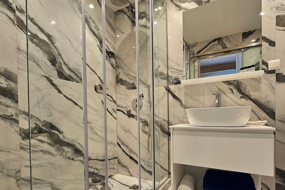A modern bathroom with a glass-enclosed shower, marble walls, and a white vanity with a sink.