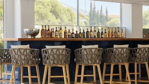 A bar area with a long counter, multiple stools, and a variety of bottles. - Paradise Resort Evia (Eretria)