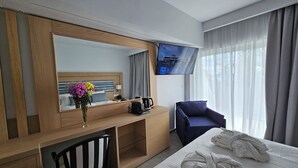 A hotel room with a bed, a desk with a chair, a TV, and a window with curtains. - Paradise Resort Evia (Eretria)