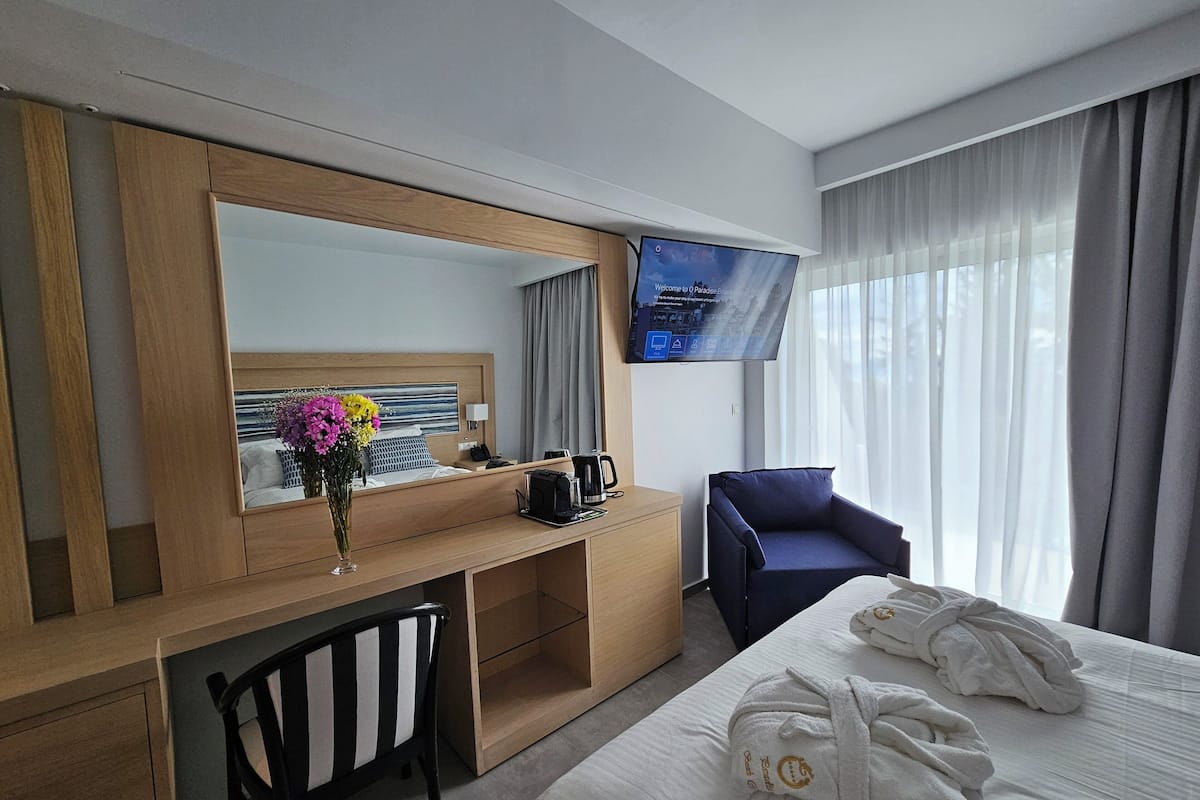 A hotel room with a bed, a desk with a chair, a TV, and a window with curtains.