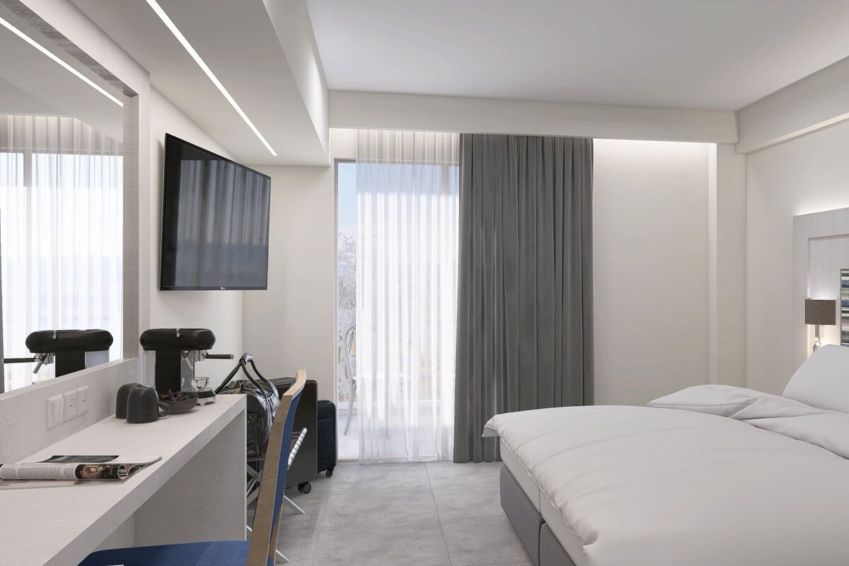 Una habitación de hotel moderna con cama, escritorio, computadora, televisor y ventana con cortinas.
