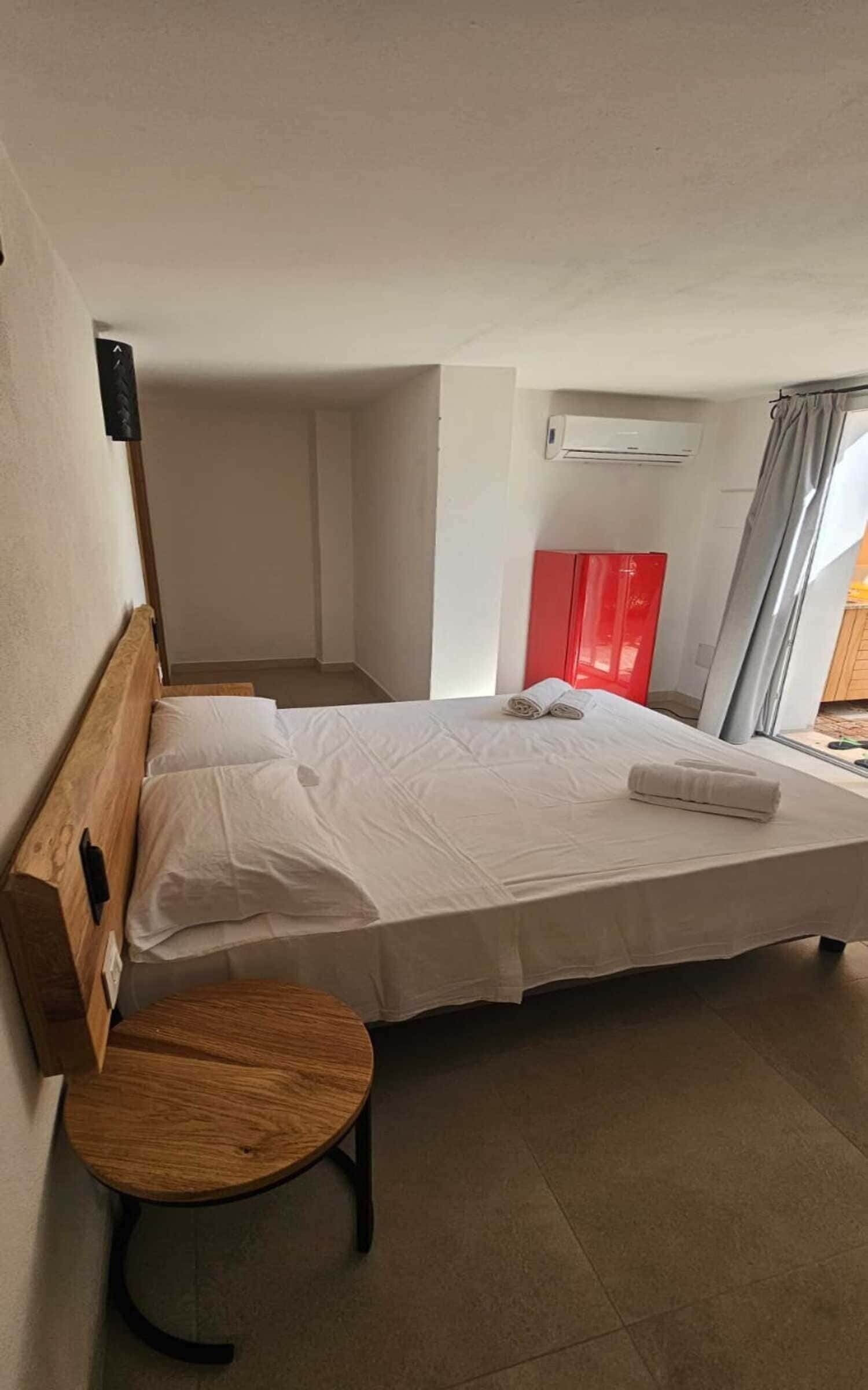 A single bed with white linens, a wooden headboard, a small round wooden table, and a red cabinet.
