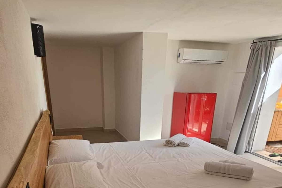A single bed with white linens, a wooden headboard, a small round wooden table, and a red cabinet.