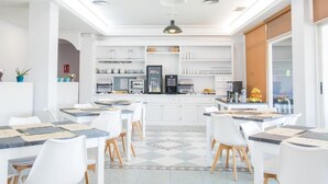 A modern kitchen with white cabinets, a central island, and a dining area with white chairs and tables. - Alda Arteixo (Abegondo)