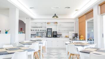 Una cocina moderna con armarios blancos, una isla central y un comedor con sillas y mesas blancas.