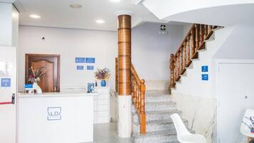 Un área de recepción con una escalera de mármol, un mostrador de recepción y una barandilla de madera.