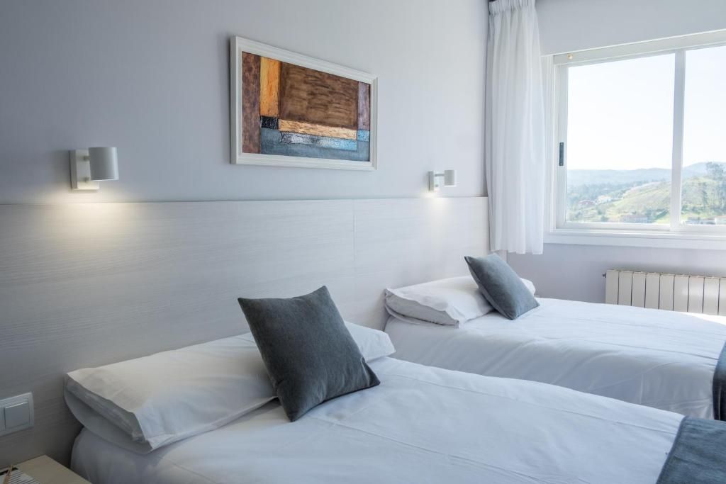 A hotel room with two beds, a window with a view, and a painting on the wall.