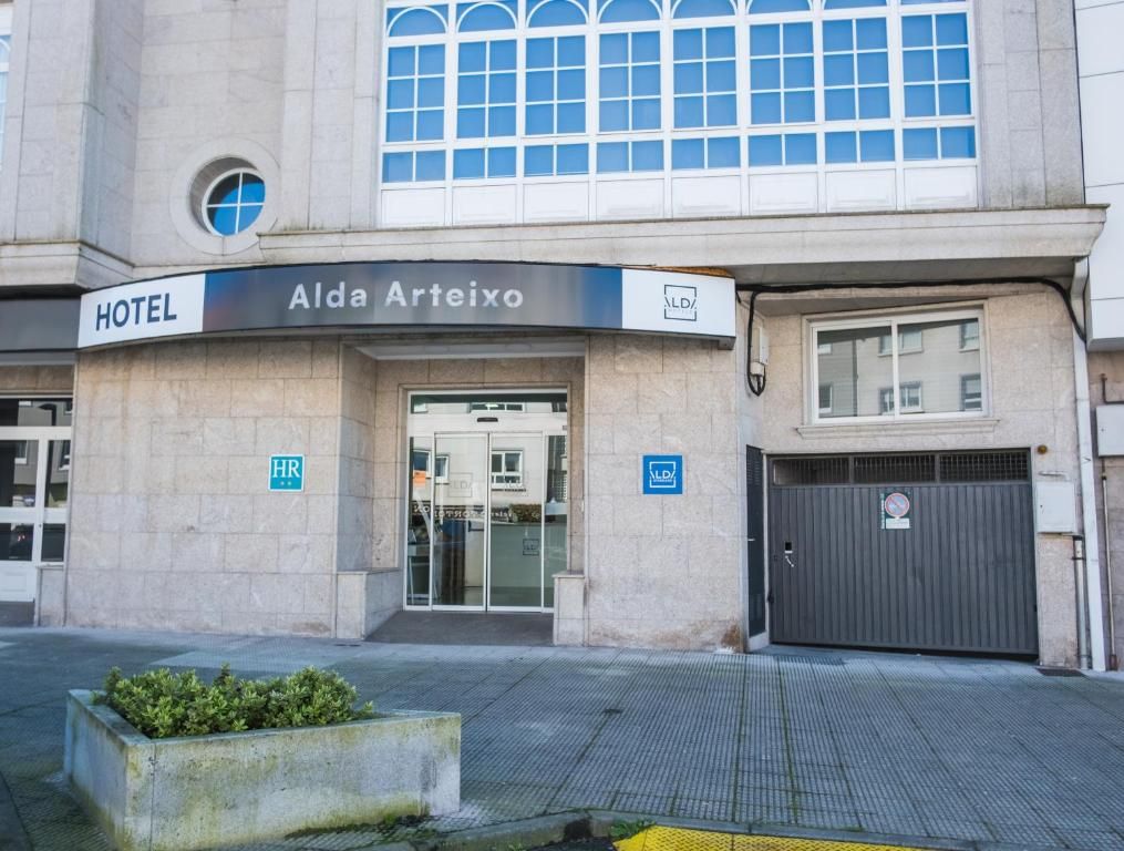 A hotel entrance with a sign reading 'Alda Arteixo HOTEL,' a wheelchair accessibility symbol, and a closed garage door.
