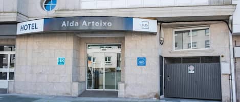 A hotel entrance with a sign reading 'Alda Arteixo HOTEL,' a wheelchair accessibility symbol, and a closed garage door.