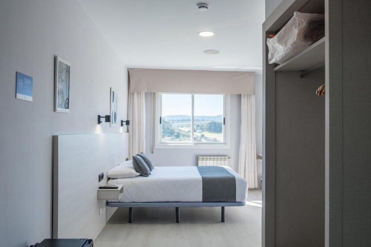 A modern bedroom with a bed, a window with a view, and a door leading to a bathroom.