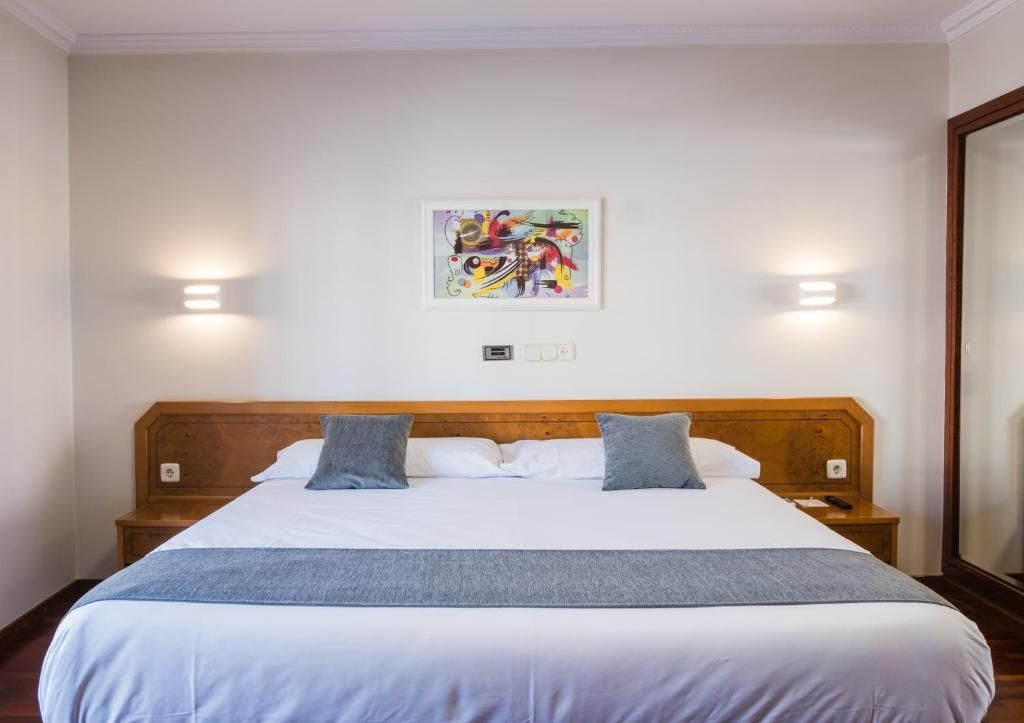 Habitació d'hotel amb un llit gran, dues taules de nit, una obra d'art penjada a la paret i dues làmpades de paret.