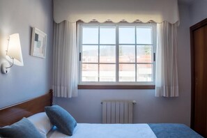 A bedroom with a large window, a radiator, and a bed with pillows. - Alda Arteixo (Abegondo)