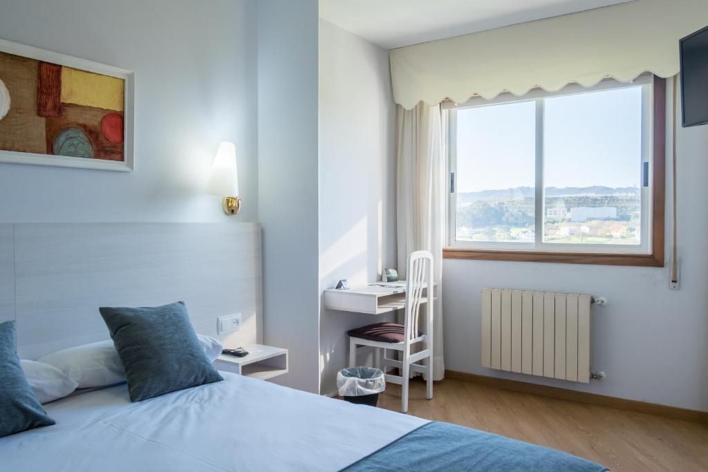A bedroom with a bed, a desk, a chair, a radiator, and a window with a view.