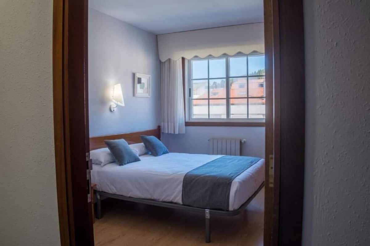 A bedroom with a bed, a window, a radiator, and a wall-mounted light fixture.