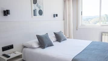 Een moderne hotelkamer met een groot bed, een nachtkastje met een afstandsbediening, een lijst met een kunstwerk aan de muur, en een raam met uitzicht.